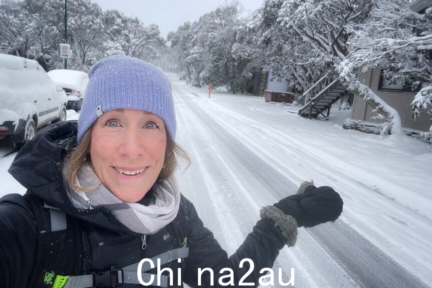 A smiling woman in a beanie stands on the side of a snow-covered road.