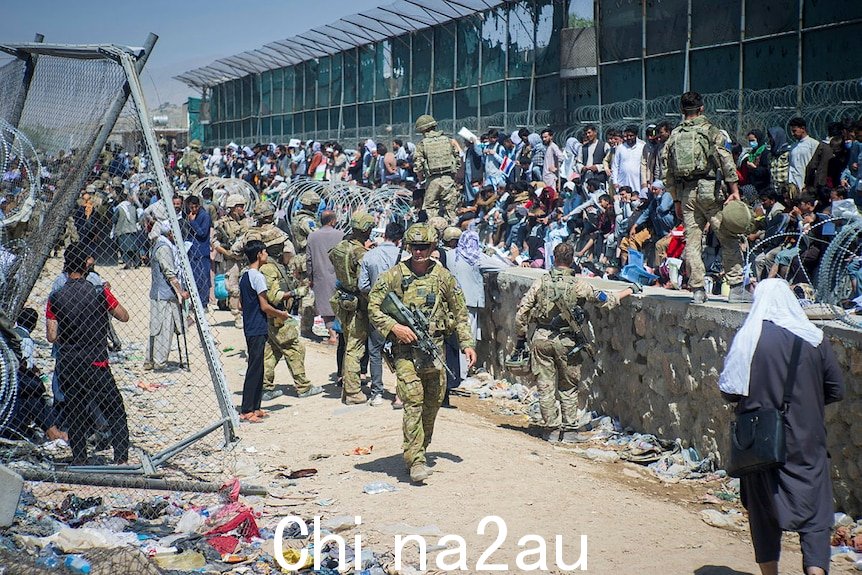 Soldiers in military uniform patrol as swathes of people congregate along a wall