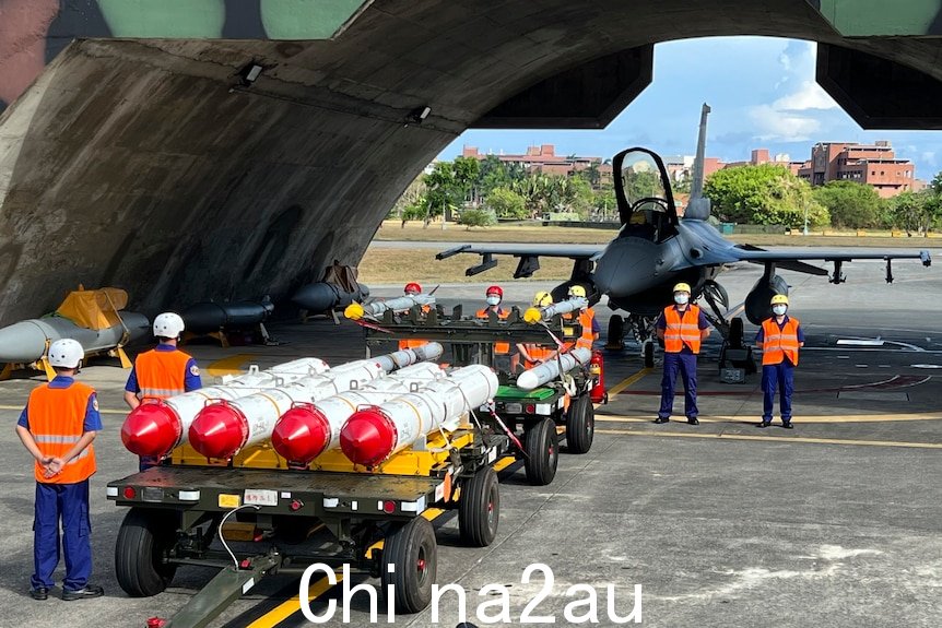 Military personnel stand beside anti-ship missiles and a fighter jet.