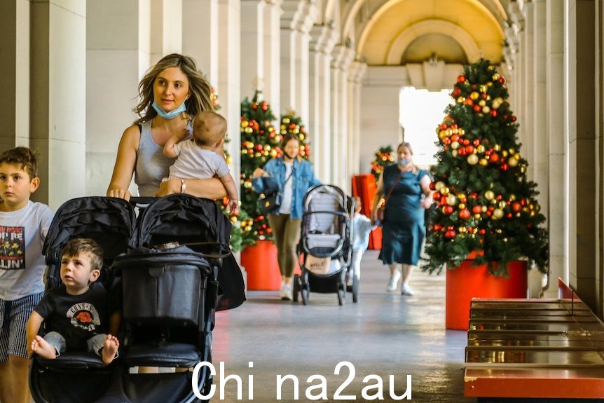 A mother walks with three children and a pram through an archway at the General Post Office, with Christmas tree.