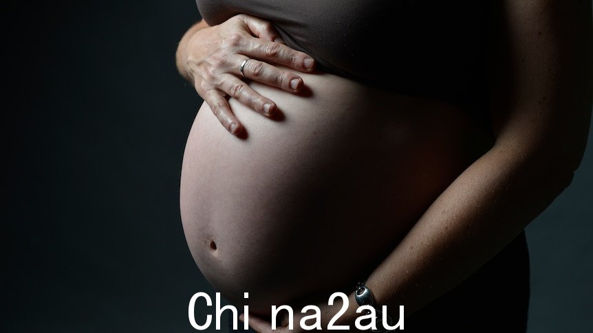 A woman's pregnant belly against a black background. 
