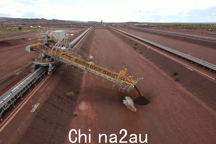 A crane pours out red dirt into a long rectangular hole.