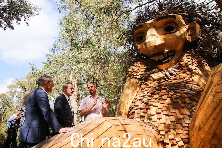 三个男人站在一个巨大的木雕旁边