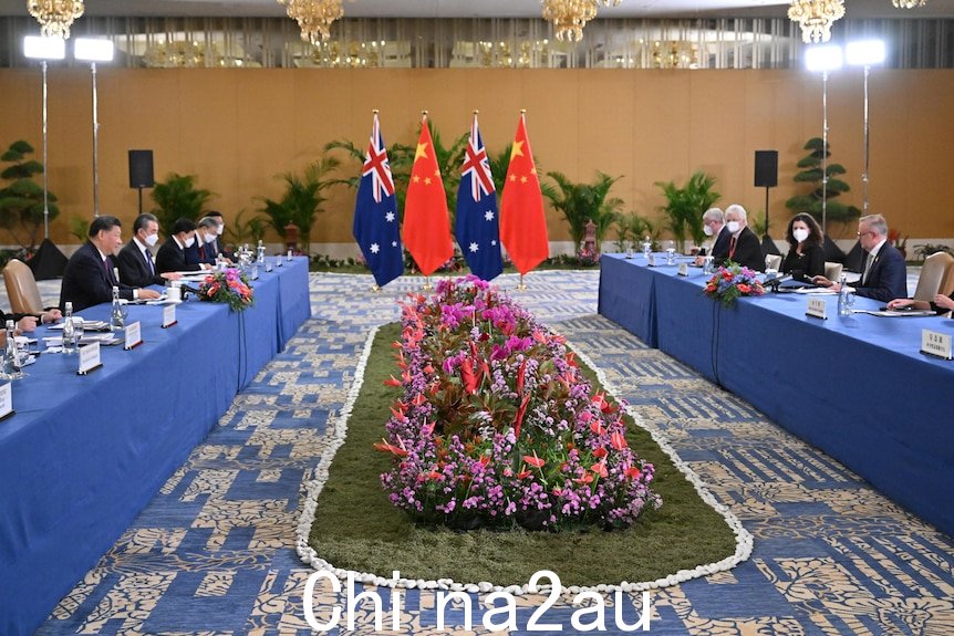 两张蓝色长桌旁坐着一群人，桌子中间摆着鲜花和澳大利亚和中国国旗