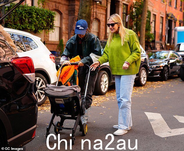 玩得开心:这位 Vogue 封面明星将她的太阳镜夹在上衣领口,推着她八个月大的儿子推着婴儿车穿过城市,同时和朋友聊天