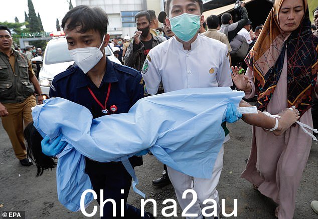 医务人员用床单抬着一名在印度尼西亚地震中丧生的男孩的遗体