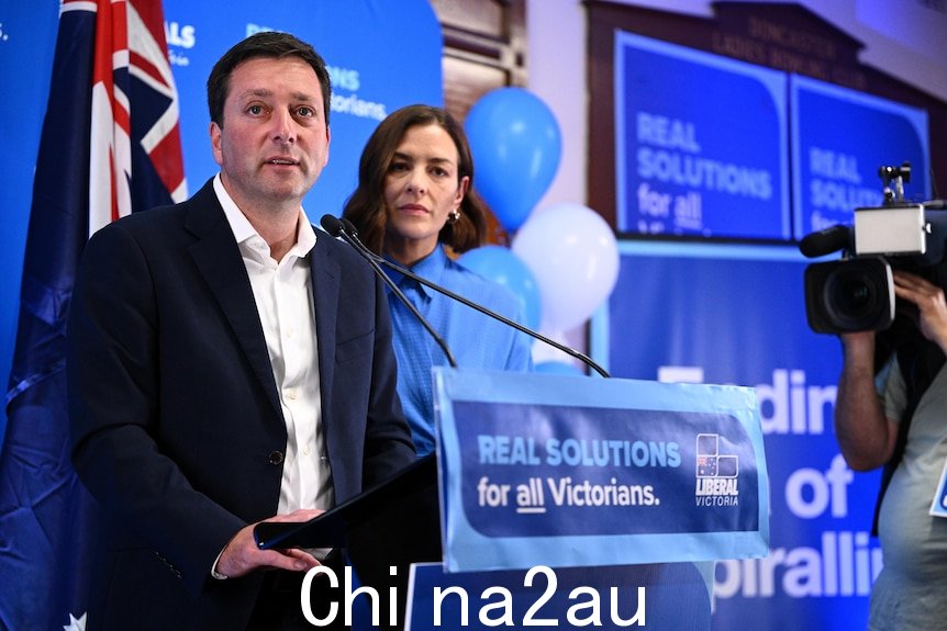 维多利亚反对党领袖马修盖伊站在他身穿蓝色衣服的妻子旁边的讲台上。