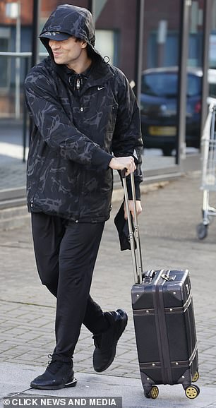 Luggage-laden:这位真人秀明星将他的兜帽盖在棒球帽上,拖着一个小手提箱,背着一个黑色背包