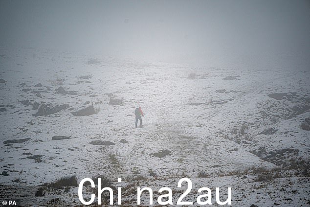 布雷肯比肯斯国家公园下雨时,一名徒步旅行者在冰雪覆盖的山丘上进入云层, Wales