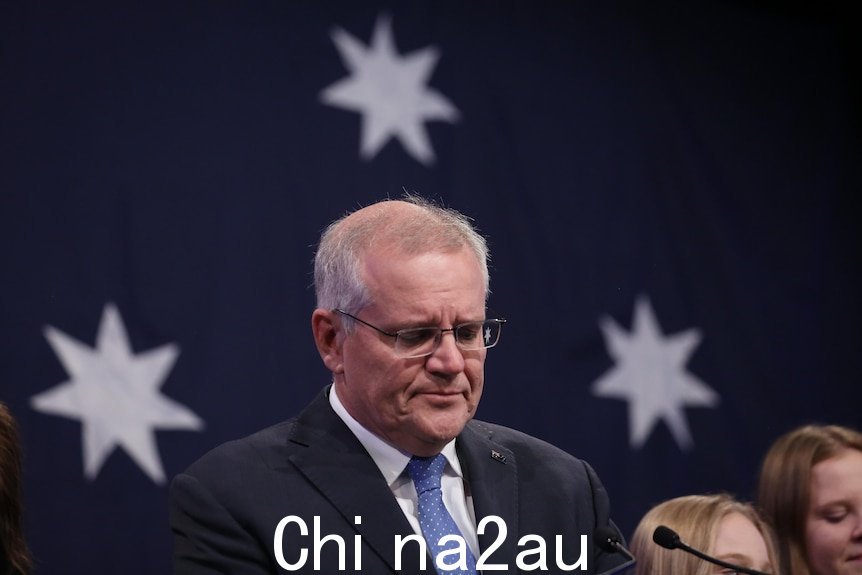 即将卸任的总理斯科特莫里森在 2022 年联邦大选后站在澳大利亚国旗前，看起来闷闷不乐。