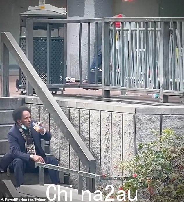 镜头拉近到一个坐在台阶上看表演的男人,他似乎正在痛饮一瓶棕色酒