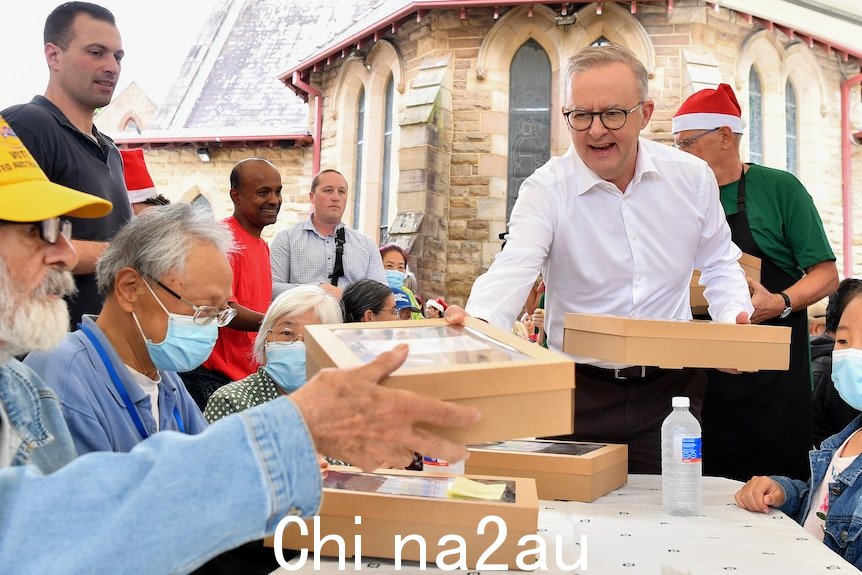 Anthony Albanese in一件白衬衫在悉尼 Rev Bill Crews 向餐桌旁的人们分发午餐