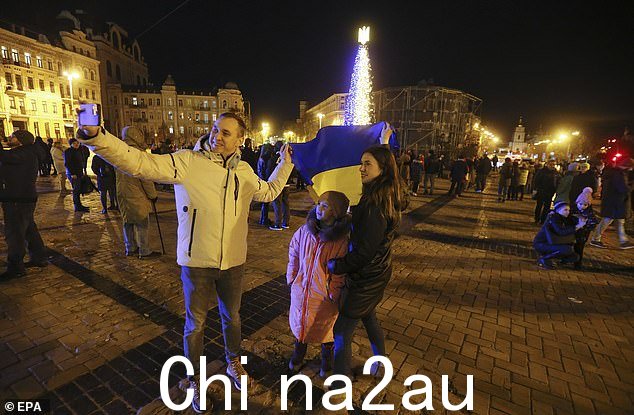 乌克兰人于 2022 年 12 月 31 日在新年之前的晚上在乌克兰基辅市中心的圣诞树附近用乌克兰国旗自拍