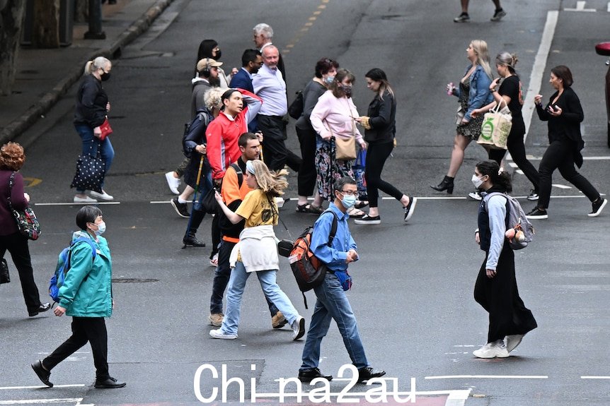 很多人，有些戴着口罩，走过马路。