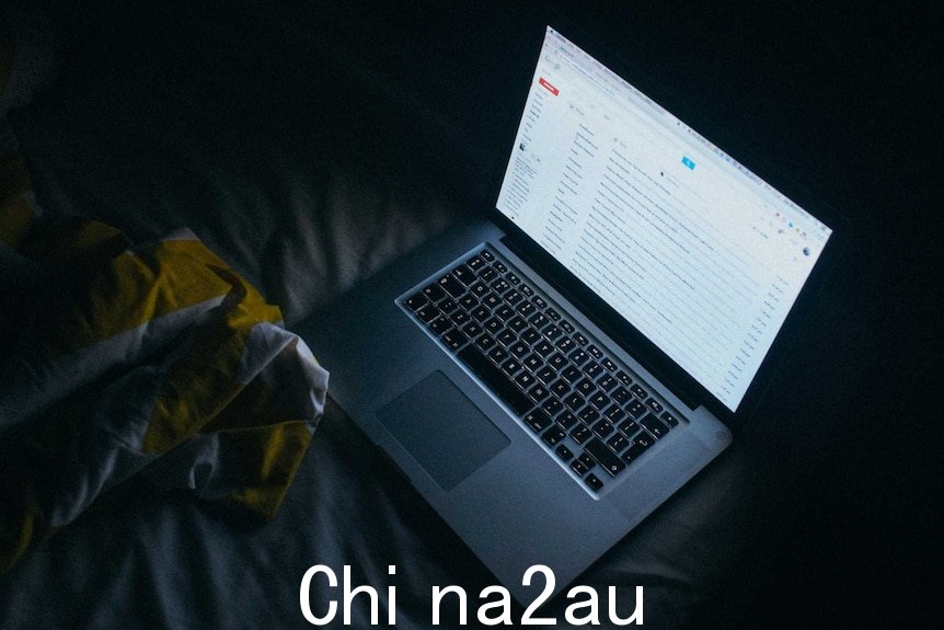 一台笔记本电脑打开放在黑暗房间的床上，屏幕上显示一个电子邮件帐户。