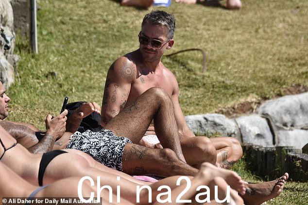 畅游一番后,Thomas 走到他的沙滩巾边,一边和一位男性朋友躺在阳光下晒干身体