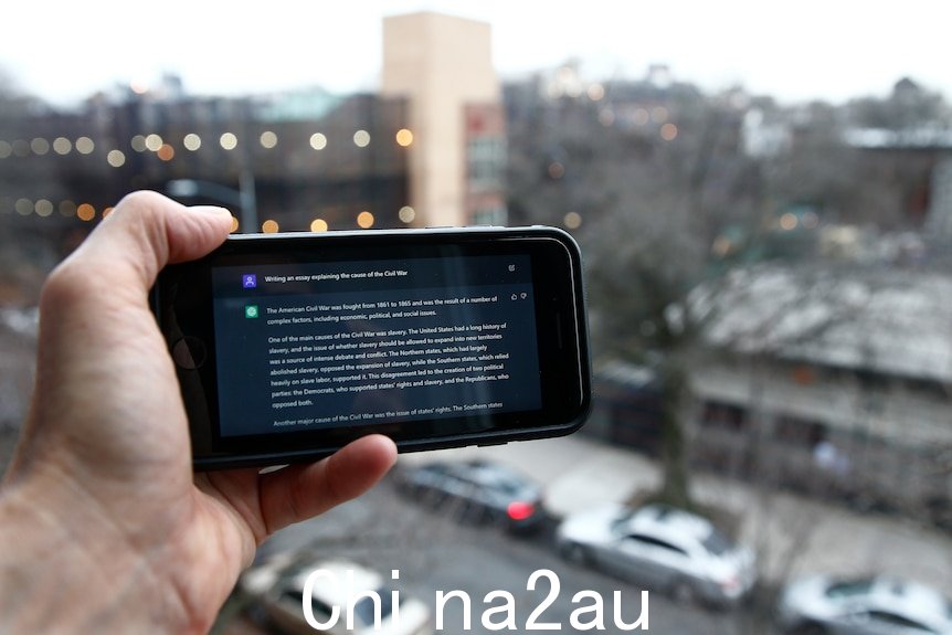 一只手拿着一部电话，在纽约市视图前显示 ChatGPT 提示. 