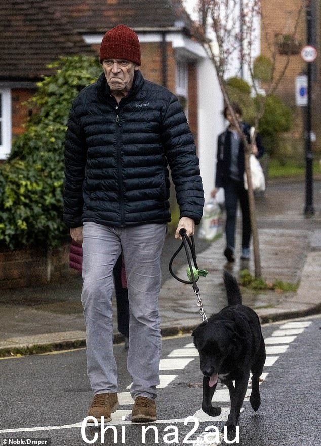 Hugh Laurie,照片中戴着一顶红色的帽子,被发现在散步时带着一种轻微的下流狗表情