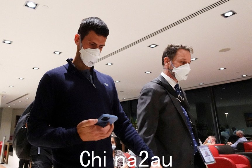 两个男人戴着口罩走路。左边的男人低头看手机。