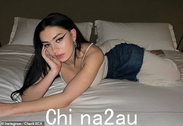 庆祝!在性感图片中,Charli 躺在床上时闪过她丰满的乳沟,穿上透明的白色连衣裙