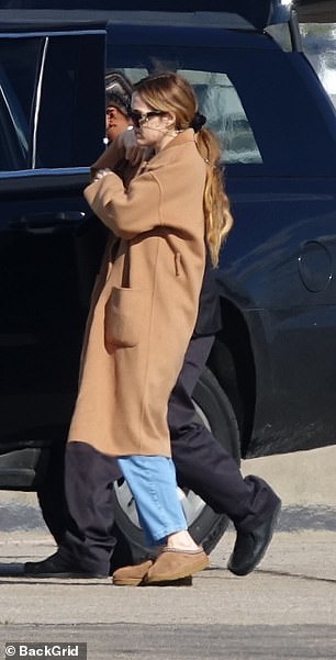 这位女演员在黑色短裤外穿了一件米色长外套,搭配蓝色牛仔裤和米色鞋子,背着一个黑色包