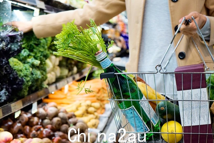 一个人在澳大利亚杂货店购物，篮子里装满了苏打水、水果和蔬菜。