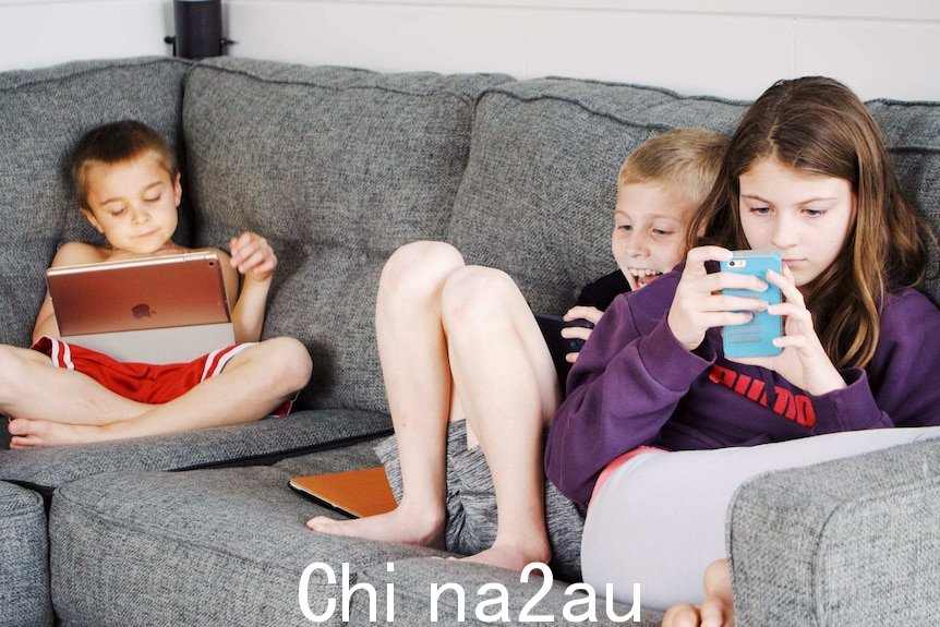 三个小孩坐在沙发上，全神贯注于手机和平板电脑。