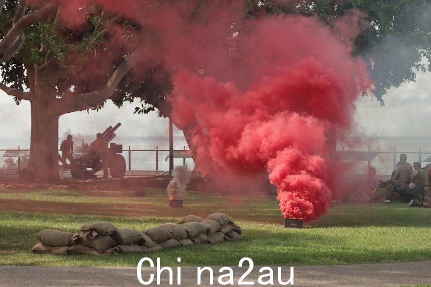 一团红色的烟雾从草地上的一个小容器中滚滚而出达尔文滨海大道，士兵们在一旁观看。” width=