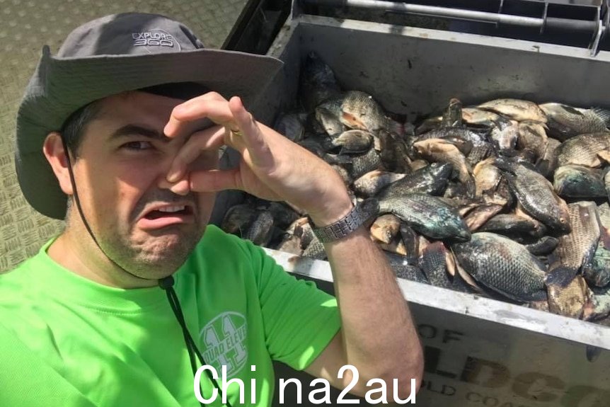 一个男人用鼻子捂着装满死鱼的垃圾箱。