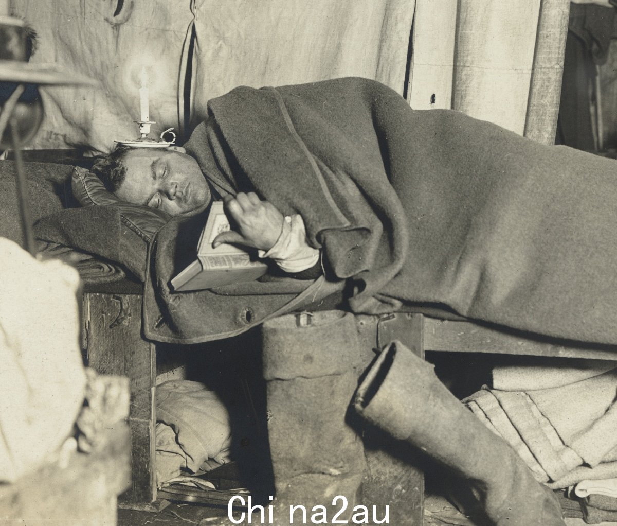 一个男人躺在床上，盖着毯子看书。 