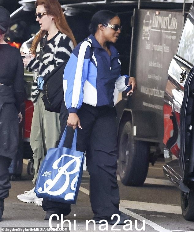 Keisha,38 岁,身穿海军蓝色运动服和太阳镜,保持低调 - 并投掷了一个 oversi装满英国药房Boots商品的zed包