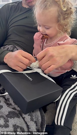 在他们分享到社交媒体网站的一段视频中,Sterling 坐在她父亲的腿上享用零食时打开了礼物