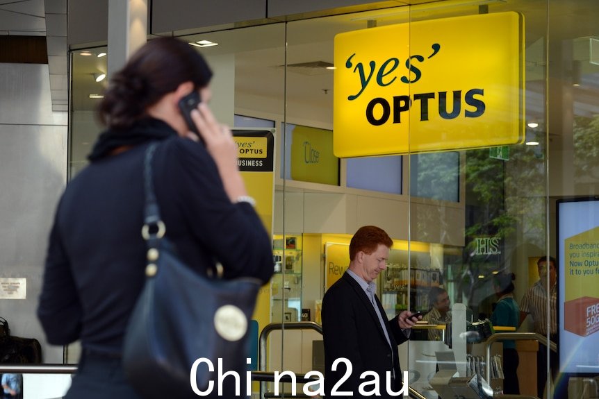 一个女人在 Optus 商店外使用她的手机，而一个男人在看他的。