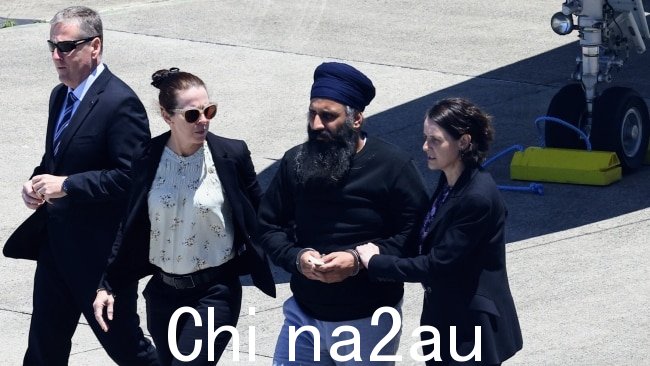 昆士兰警察和 dete在从新德里经墨尔本被引渡到凯恩斯后，工作人员护送拉杰温德·辛格从包机到凯恩斯机场等候的警车。图片：Brendan Radke