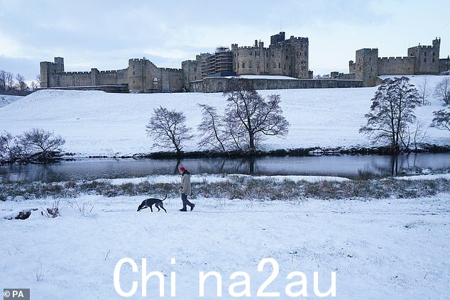 NORTHUMBERLAND:在诺森伯兰郡的阿尼克城堡,一名男子牵着他的狗穿过白雪覆盖的田野。下周英格兰和威尔士将迎来温和多变的天气