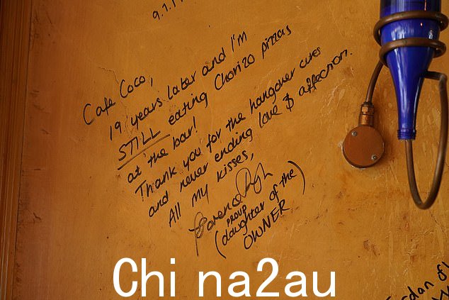 墙上写着 Florence 在 2019 年写的一条信息:'Café CoCo,19 年后我还在酒吧吃香肠披萨'