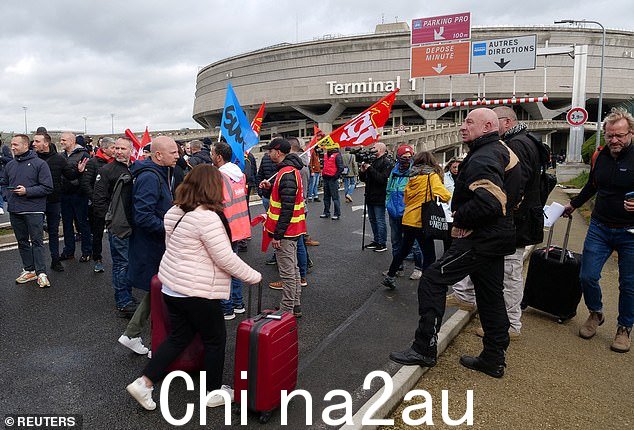图:巴黎戴高乐机场全国罢工和抗议法国政府养老金改革的第九天,罢工的机场工作人员聚集在 1 号航站楼外,乘客提着行李走在路上巴黎附近,3 月 23 日