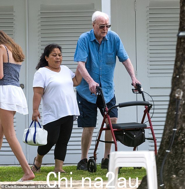 On the move: Sir Michael Caine, 90, was assisted by a walking frame and aide as he headed to the beach in Barbados on Sunday for some well earned downtime after major surgery