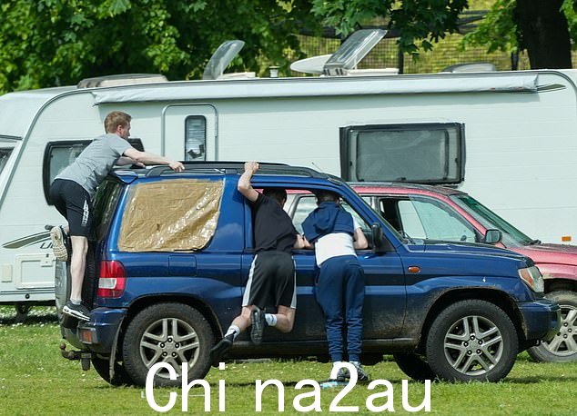 许多车辆,包括一辆看起来没有窗户的蓝色 4x4,都停在绿地上