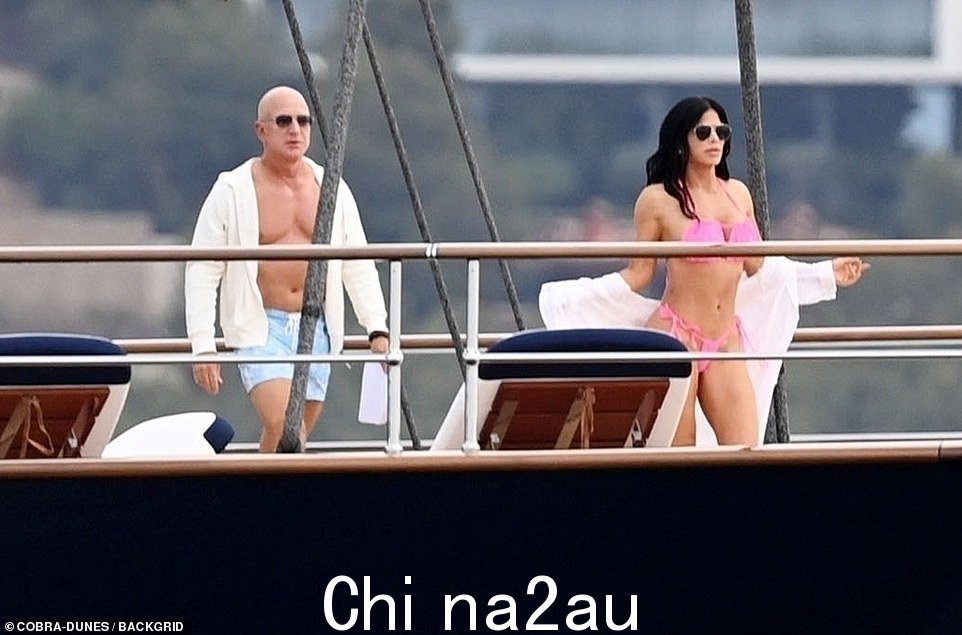 Bezos,在他裸露的胸前穿着白色连帽衫,走在女友桑切斯身后超级游艇off the coast of Mallorca