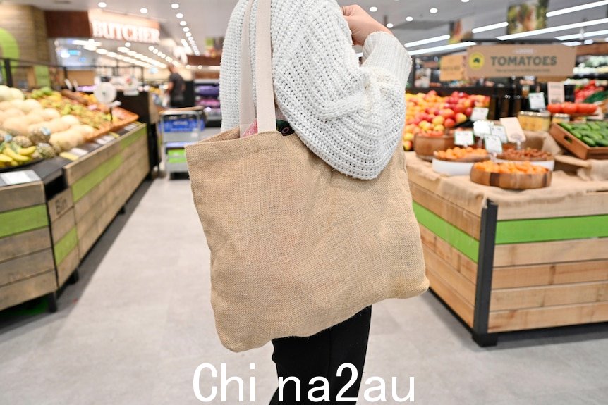 一个人身穿白色针织套衫，背着麻布手提袋在超市的生鲜区。