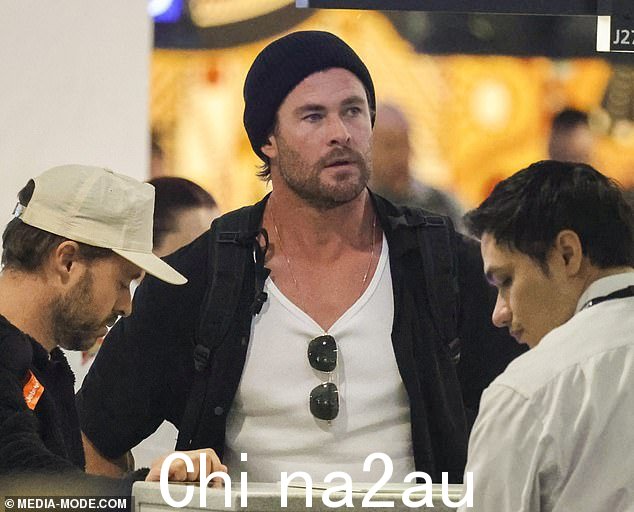 Chris 在悉尼机场漫步时穿着深色牛仔裤和开领衬衫,外搭白色背心,展示了他的浅黄色体格