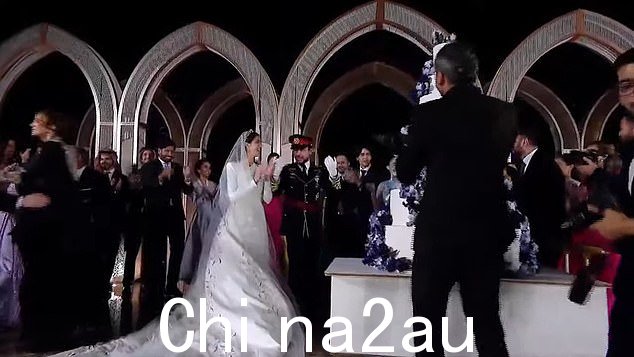 当蛋糕被推入并呈现给新婚夫妇时,人群聚集在一起观看新婚夫妇
