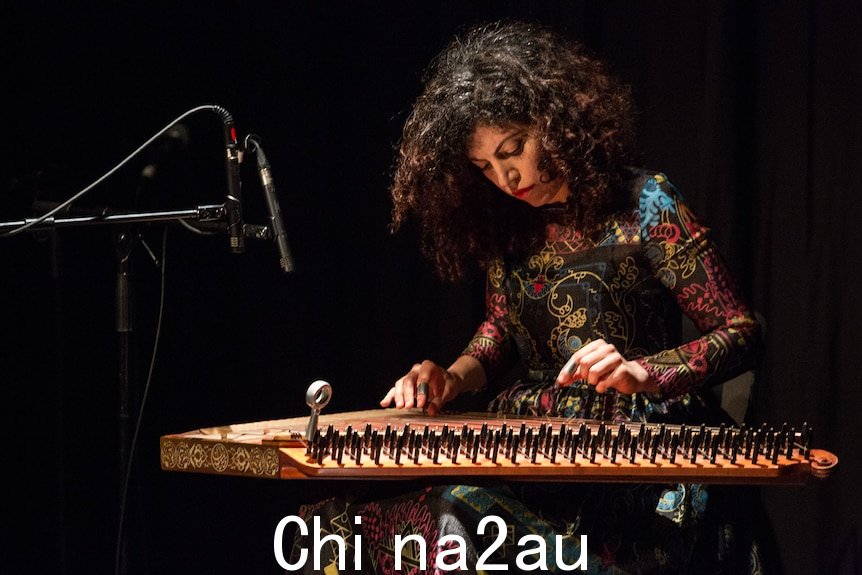 Maya Youssef 坐在舞台上表演，当她拨动琴弦时，膝盖上放着一个 qanun。