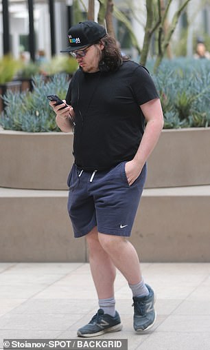 James 穿着类似的休闲装,但穿的衣服层数较少 - 穿着海军短裤、运动鞋、黑色衬衫和帽子