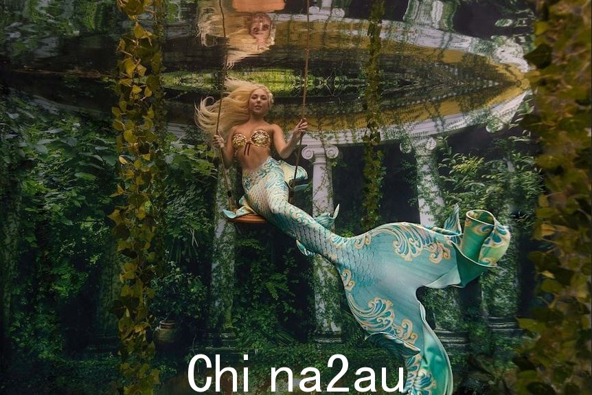 一个穿着美人鱼服装的女人在水下摇摆。” width=