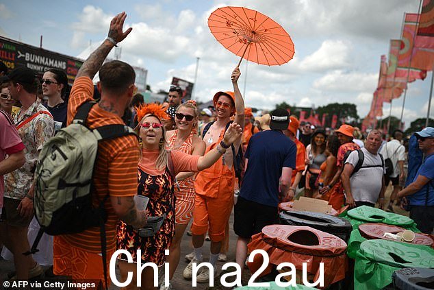 一组穿着橙色衣服的朋友在格拉斯顿伯里的节日村周围散步