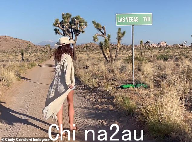 她走向一个标牌,上面写着“拉斯维加斯 170”,背景是泥土、灌木丛和沙漠树木