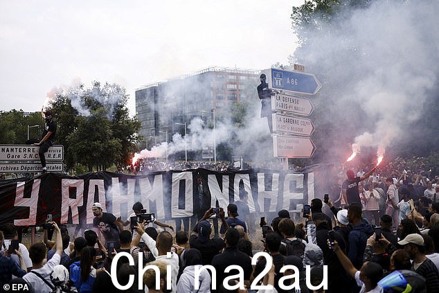 当人们参与时,可以看到一名黑衣抗议者坐在交通标志上在纪念 17 岁 Nahel 的游行中