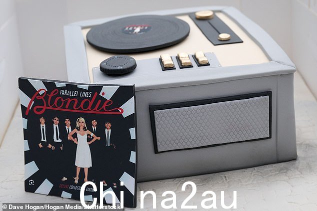 哇!这位金发女郎明星在电唱机形状的蛋糕旁边摆出灿烂的笑容,蛋糕上还放着她标志性的平行线专辑的冰镇版本